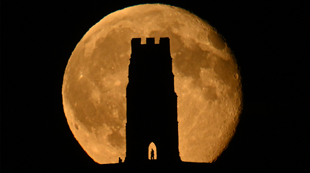 The waning Hunter's Moon is eclipsed by the ancient silhouette of St Michael's Tower atop Glastonbury Tor in Somerset.